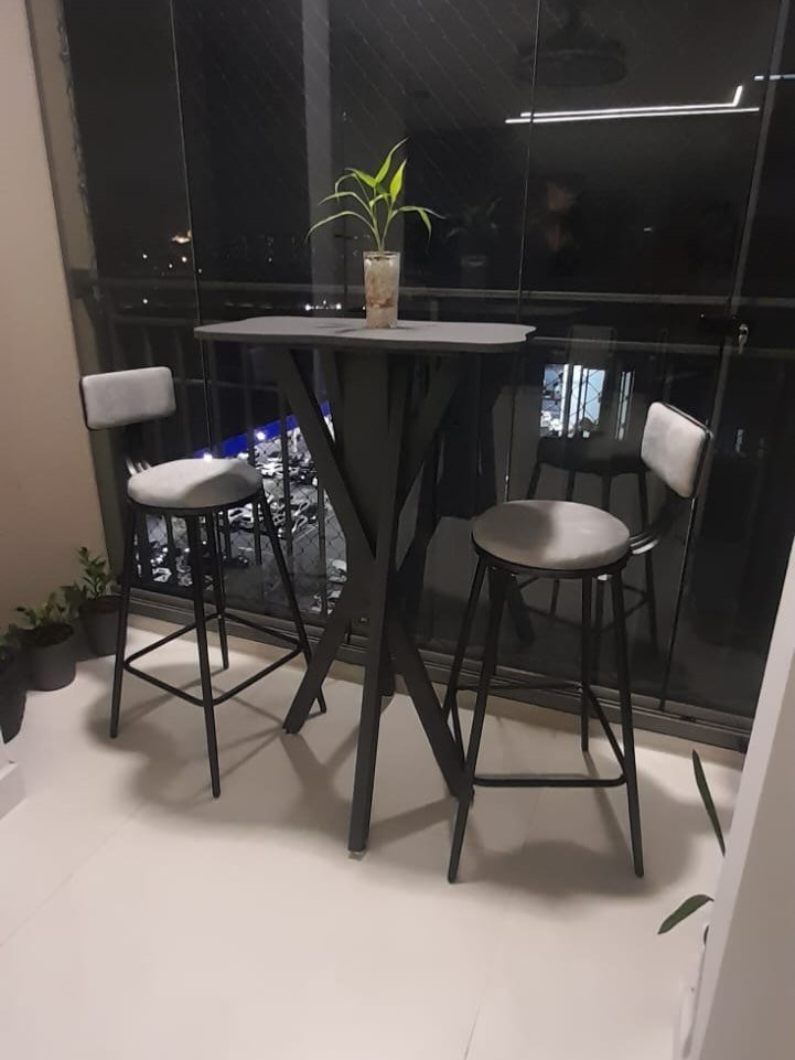 Varanda à noite com mesa alta de pés cruzados e duas banquetas