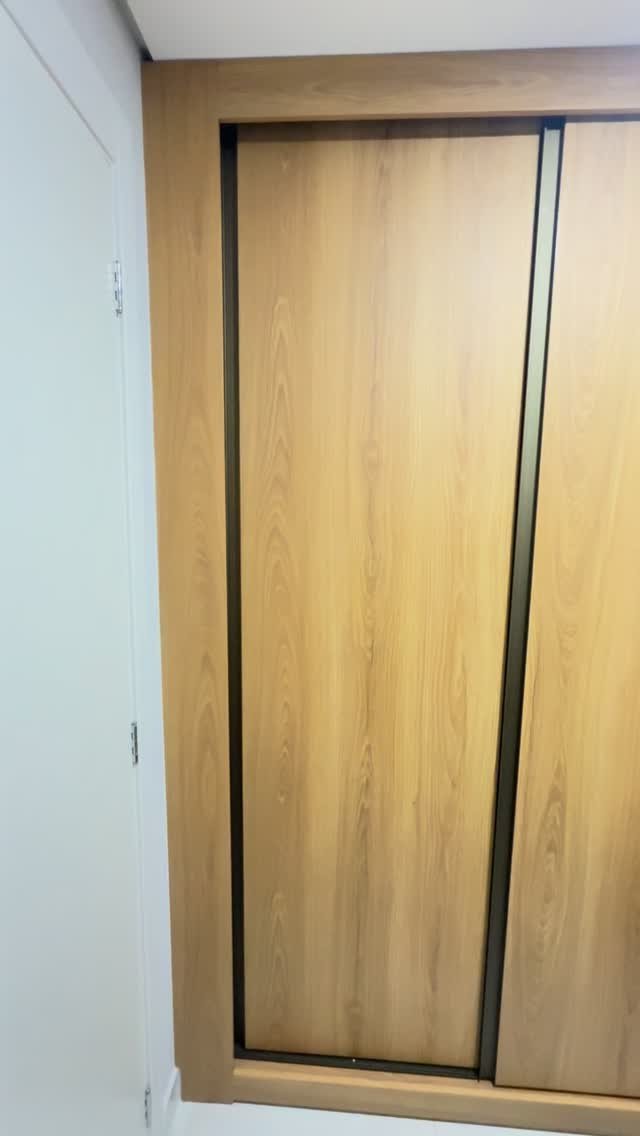 Porta de correr de guarda-roupa em madeira clara com perfil escuro entre as folhas