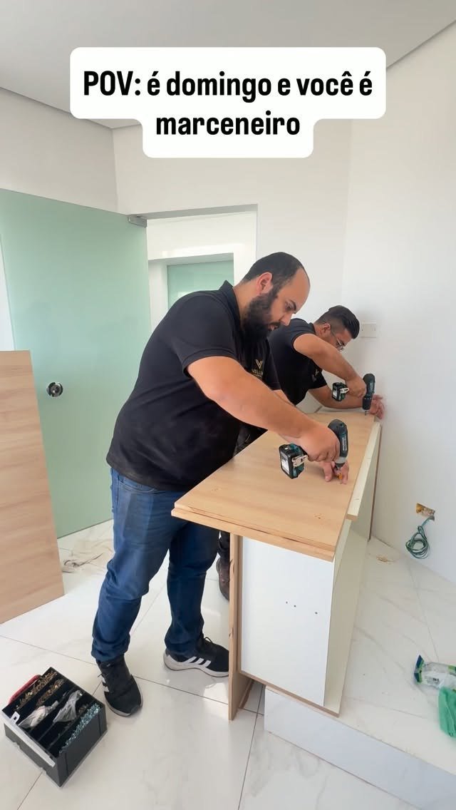 Dois montadores da Vellor, de camiseta preta com o logo, parafusando o tampo de uma bancada em madeira clara