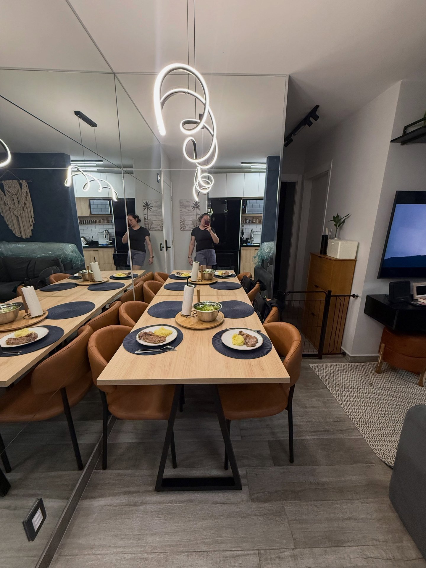 Sala de jantar com mesa de tampo em madeira clara, cadeiras caramelo e parede de espelho