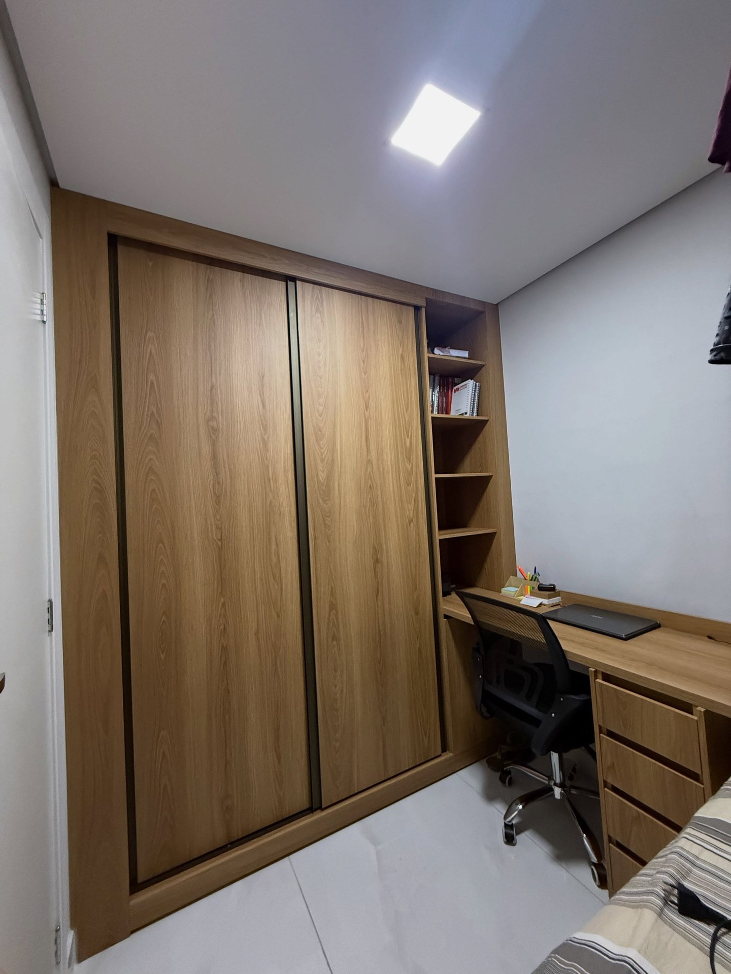 Quarto com guarda-roupa de portas de correr em madeira clara, prateleiras abertas e escrivaninha com gaveteiro